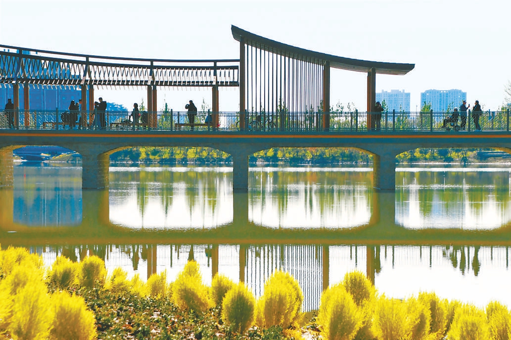 玉河濕地公園秋色繽紛、如詩如畫，市民游客在湖心廊橋上遠眺秋景斑斕。